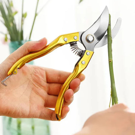 Gold-handled garden pruners being held with a blurred plant background