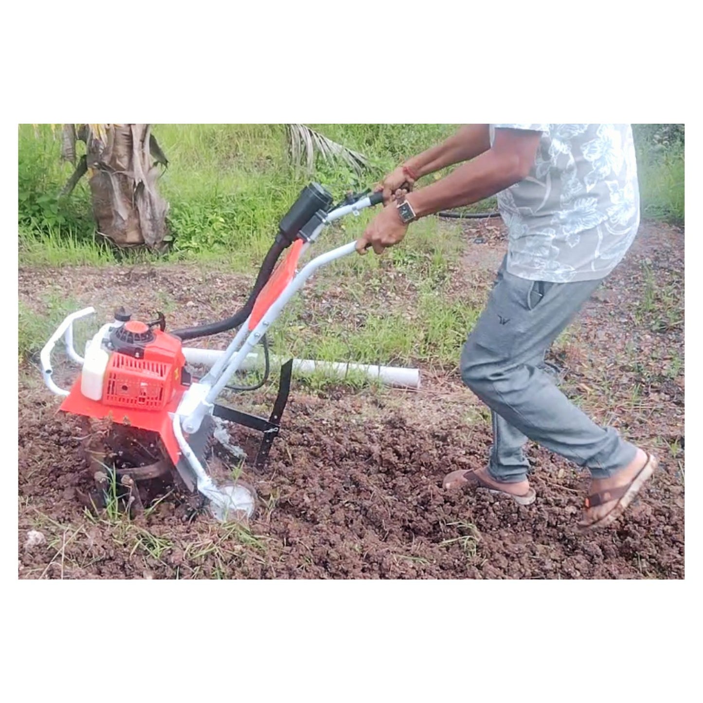 Person using a tiller on a field with a tree in the background