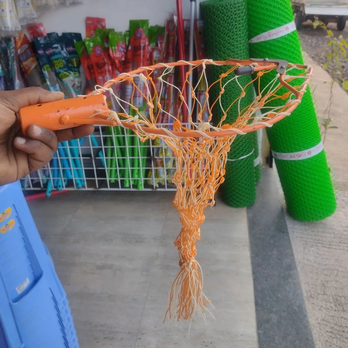 mango plucker net held by a hand with a store and green mesh rolls in the background