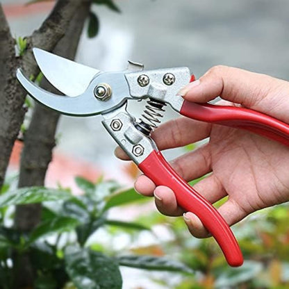 Gardening shears with red handles held by a hand against a blurred garden background
